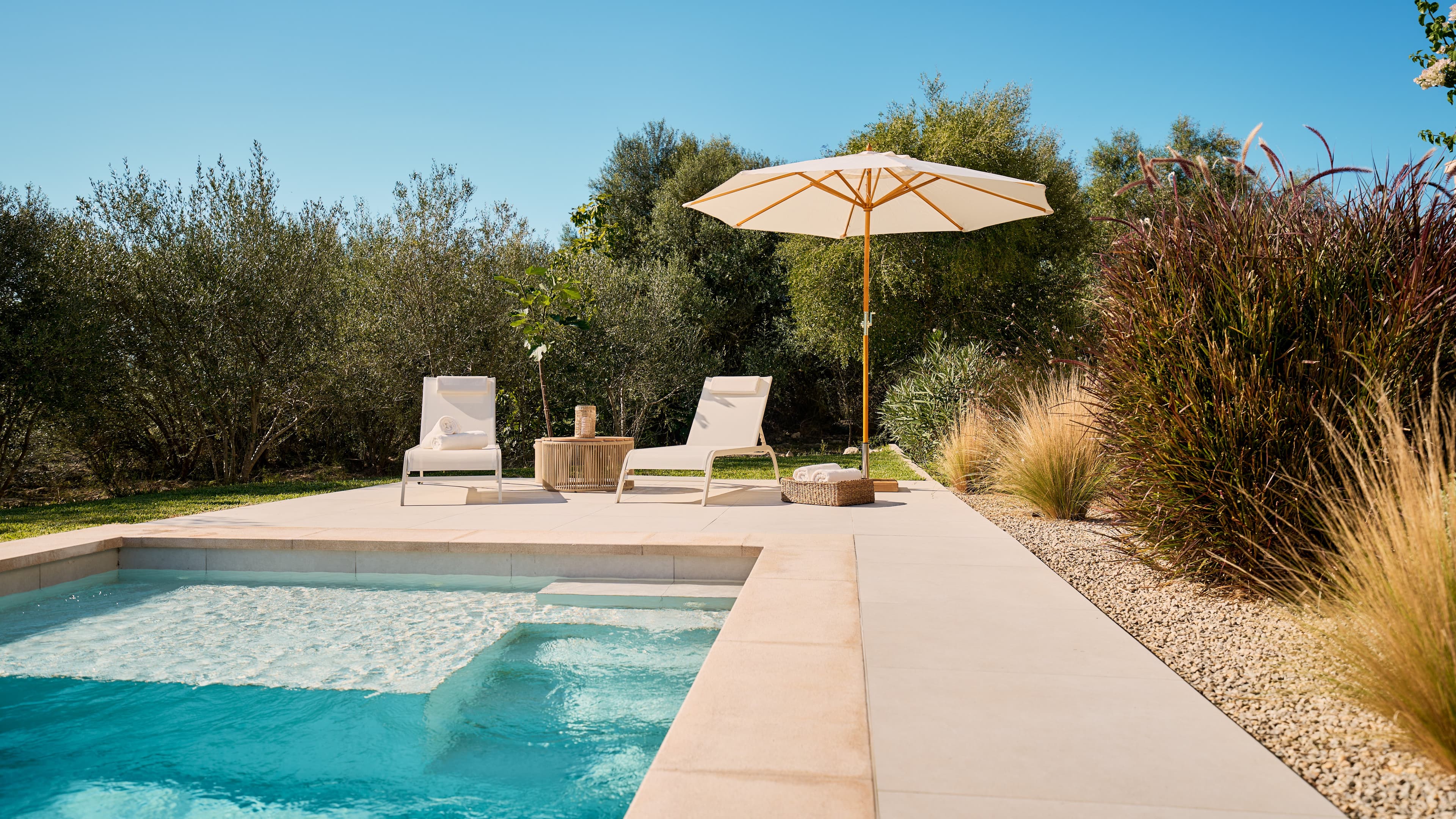 Moderner Pool im Traumhaus auf Mallorca mit türkisblauem Wasser, Sonnenliegen und Sonnenschirm – umgeben von mediterranen Pflanzen und Natur.