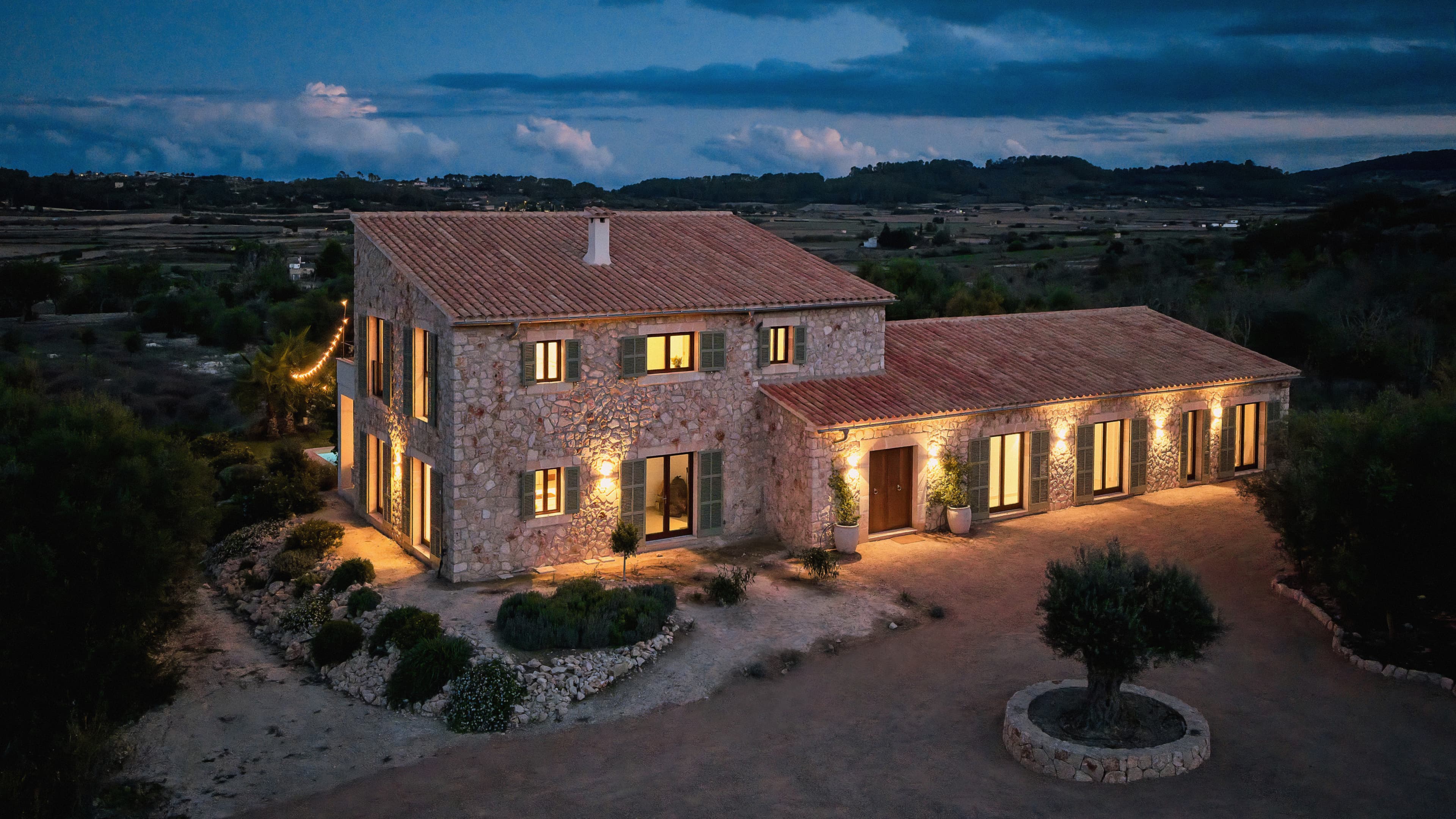 Außenansicht des Traumhauses auf Mallorca in der Abenddämmerung mit Blick auf den beleuchteten Eingangsbereich und die große Auffahrt