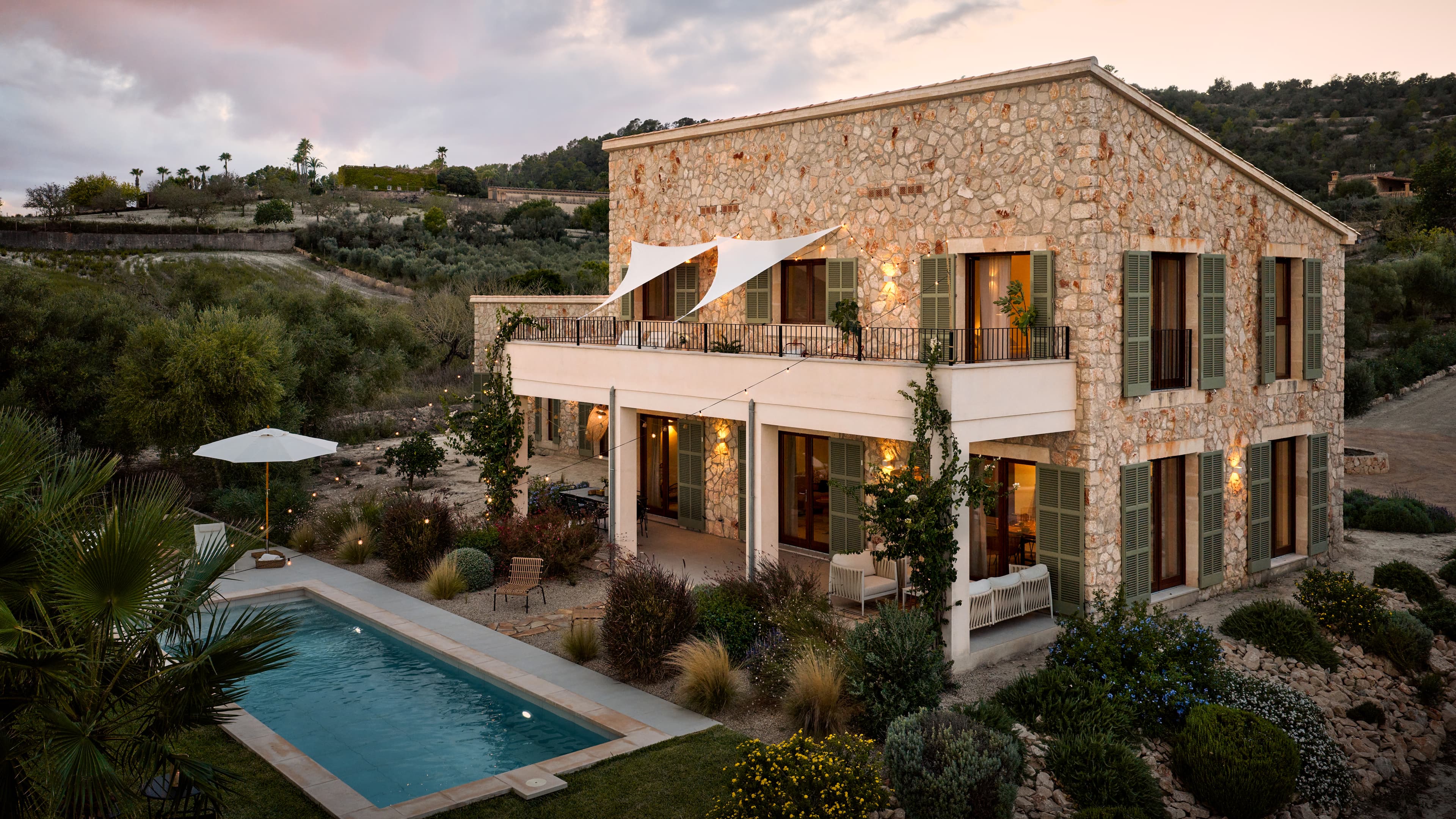 Das Traumhaus auf mallorca in der Außenansicht mit Blick auf den Pool und mediterranen Garten in der Abenddämmerung