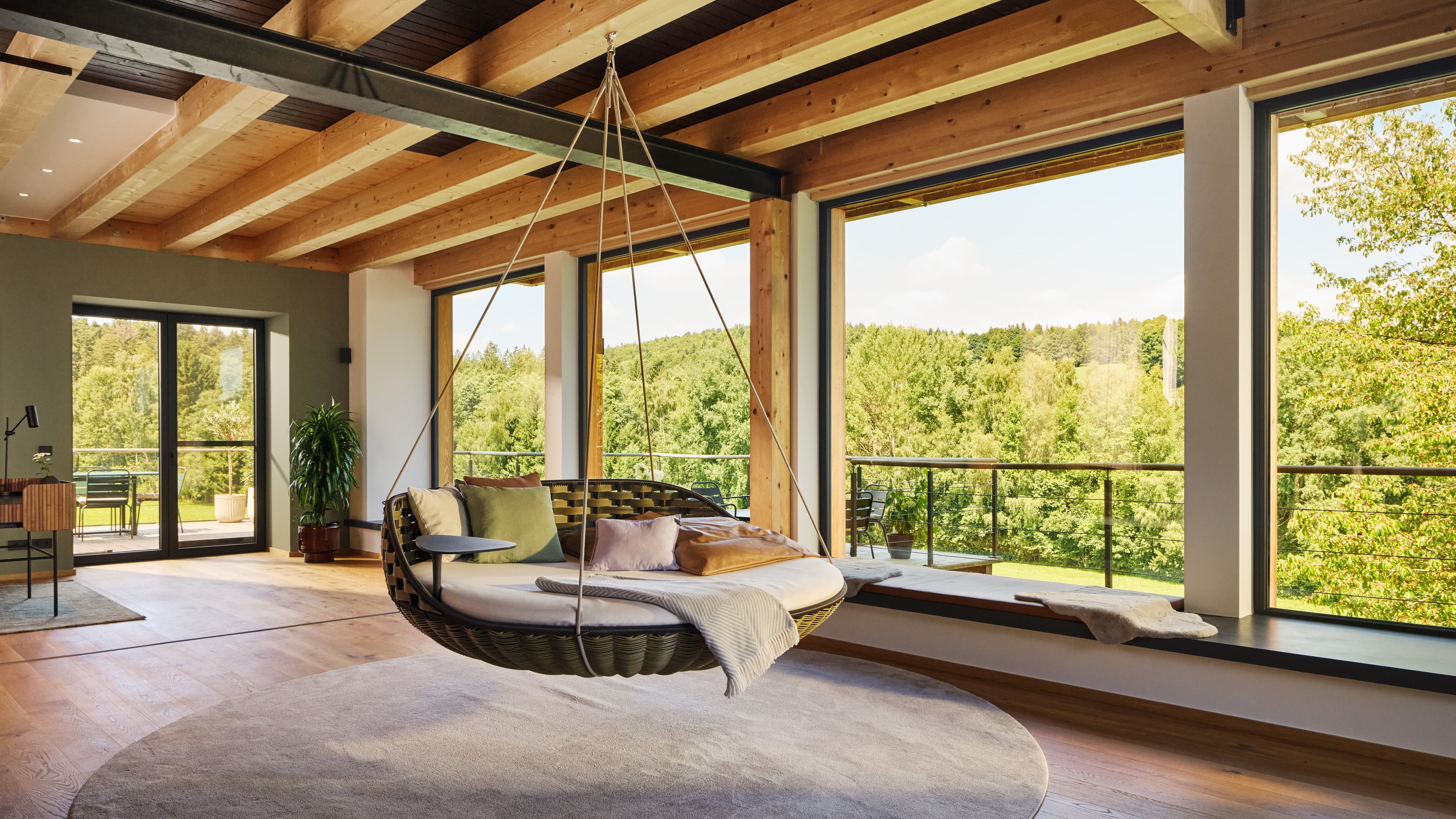 Ein freischwebender Swing-Chair umgeben von riesigen Fenster, die einen Ausblick in den Bayerischen Wald ermöglichen