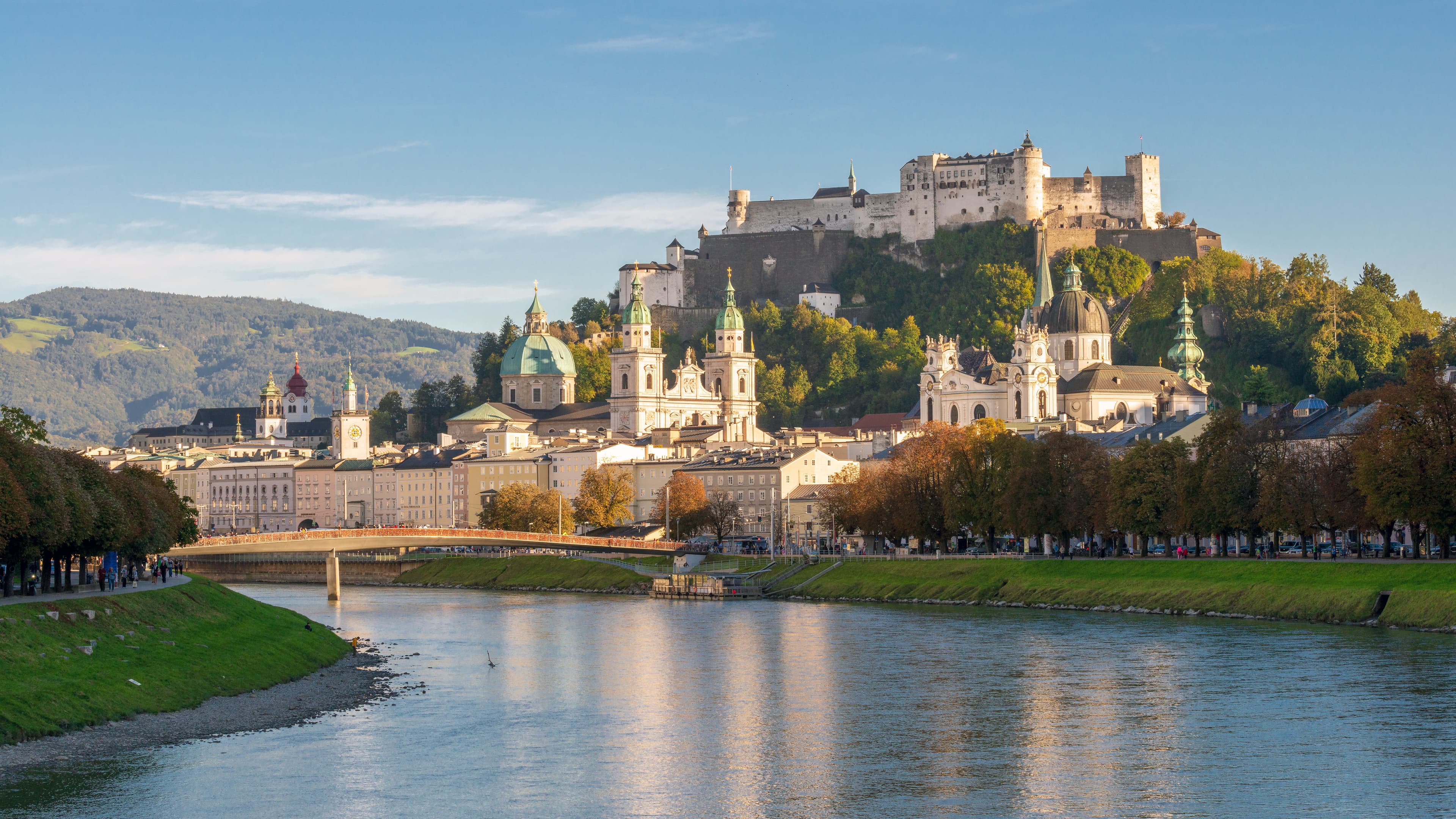 Blick vom Fluss Salszach auf das Stadtzentrum von Salzburg im Hintergund mit der Festung Hohensalzburg