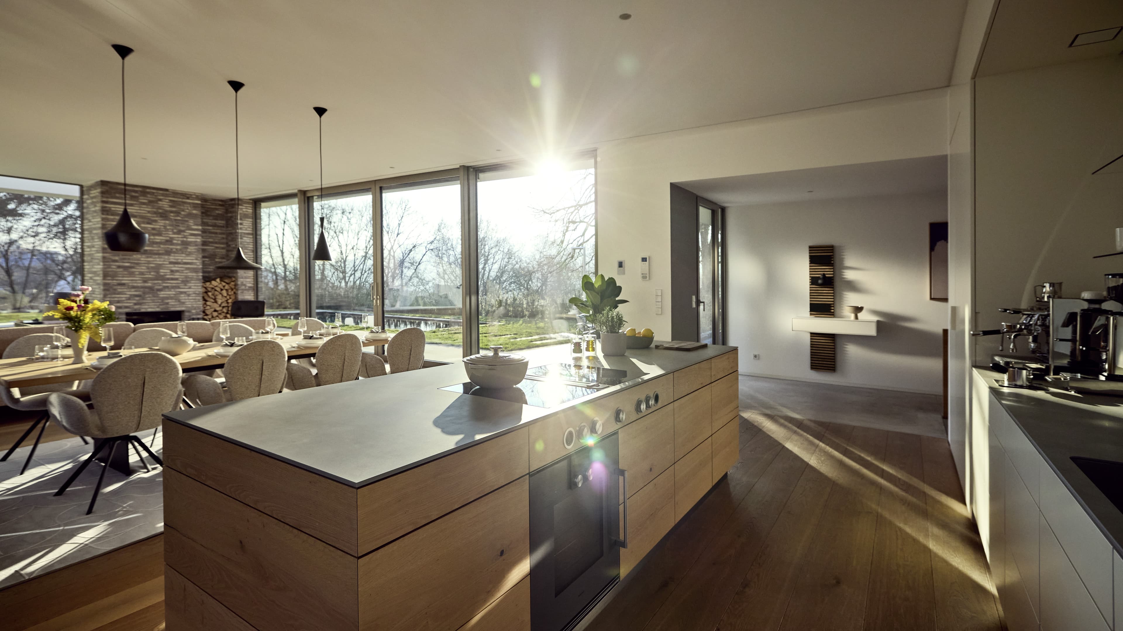 Blick in den großen offenen Wohn- und Essbereichs mit bodentiefen Fenstern und großem Esstisch